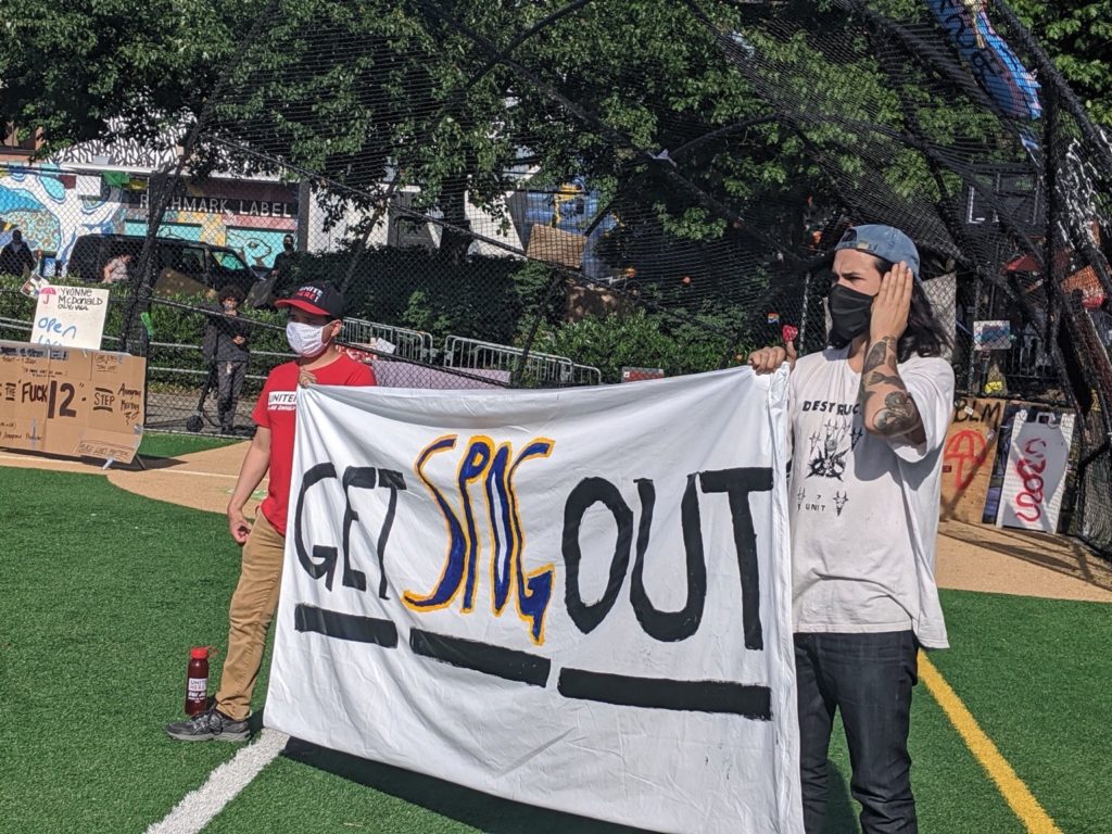 Protestors at Cal Anderson Park baseball field holding banner saying "Get SPOG Out"