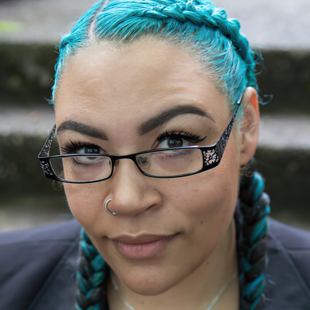 Close-up portrait photography of Sherae Lascelles with glass, blue-dyed hair in braids, glasses, and nose ring, lowing upward at camera.